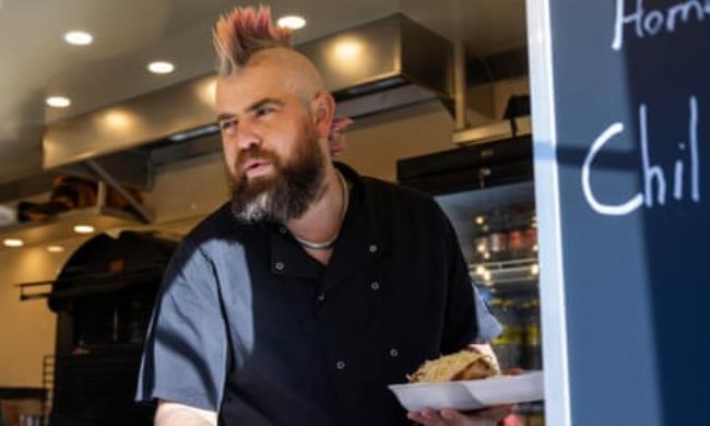A worker squeezes sauce on to a filled jacket potato in a tray
